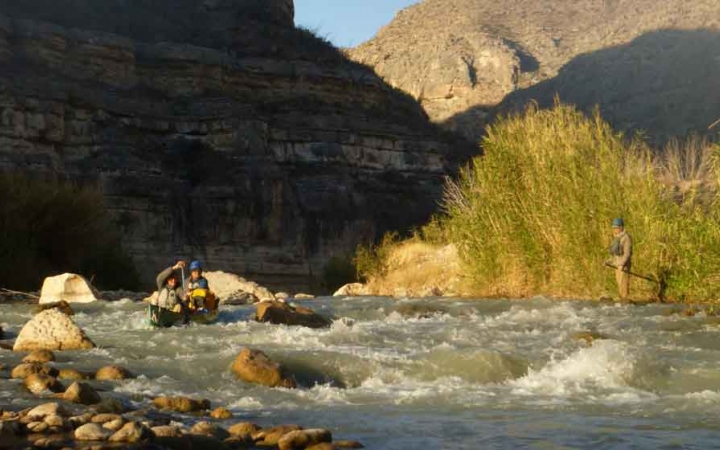 two people paddle a canoe through whitewater while high canyon walls stand in the background